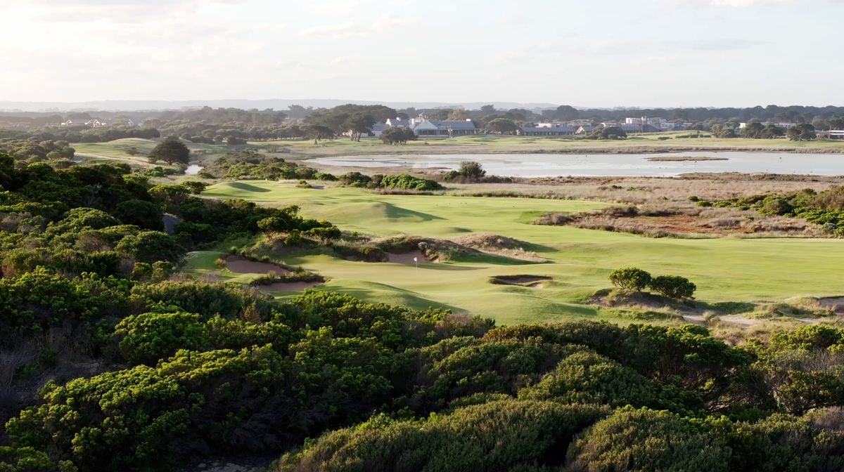 Aerial view of a green at 13th Beach Golf Links surrounded by dunes, wetlands and the clubhouse in the distance.