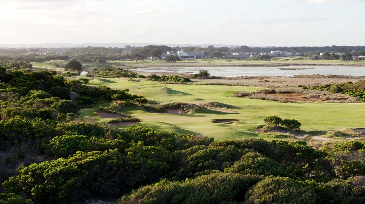 Aerial view of a green at 13th Beach Golf Links surrounded by dunes, wetlands and the clubhouse in the distance.