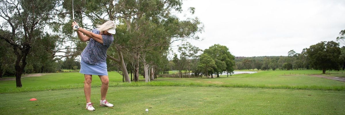 A golfer teeing off on a tree-lined fairway at Easts Leisure & Golf, with a pond visible in the distance.