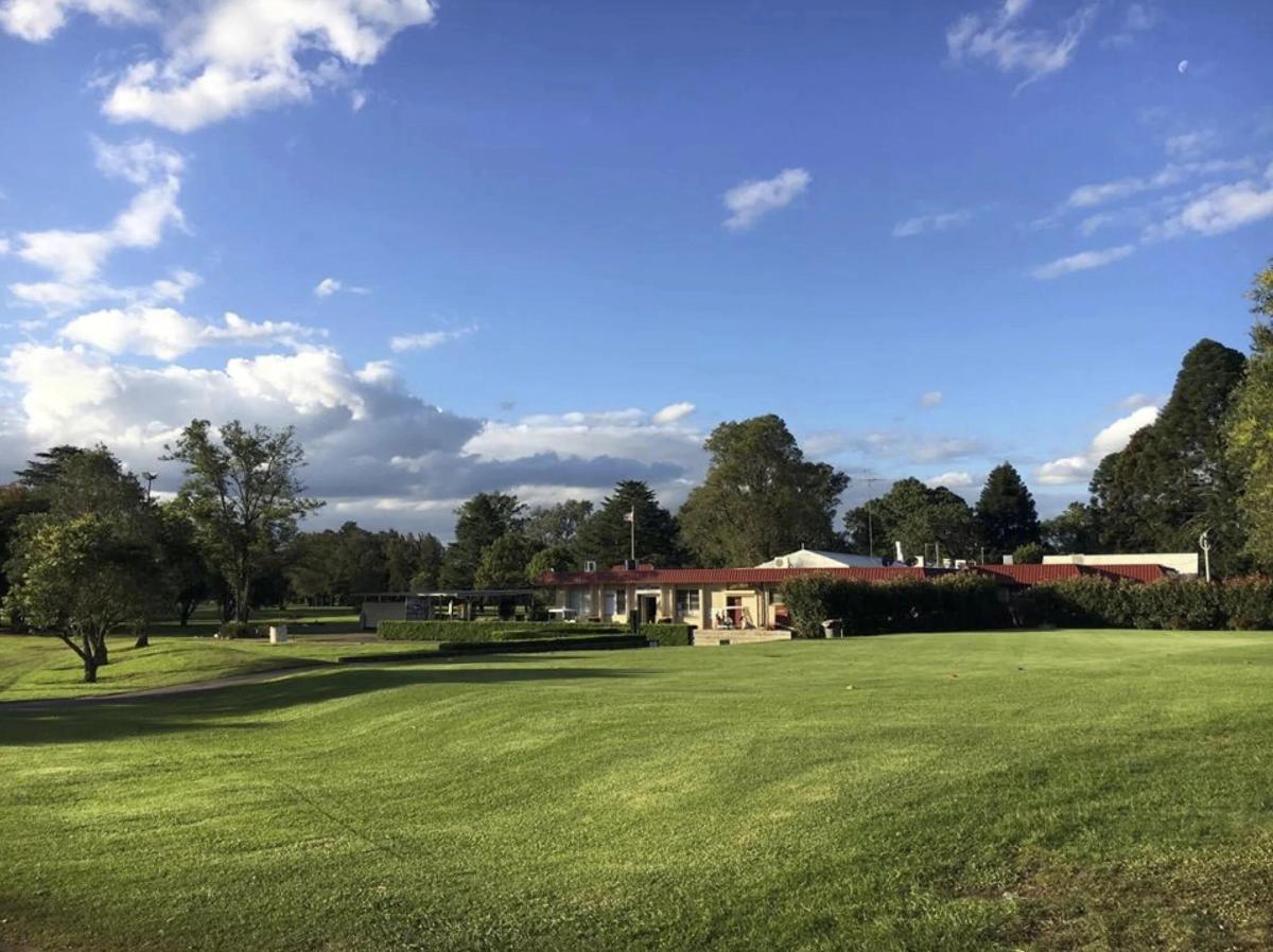 The clubhouse and fairway at Dunheved Golf Club under a blue sky with scattered clouds.