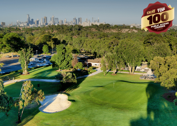 Aerial view of a green and bunker at Yarra Bend Golf course with the Melbourne city skyline visible in the distance.