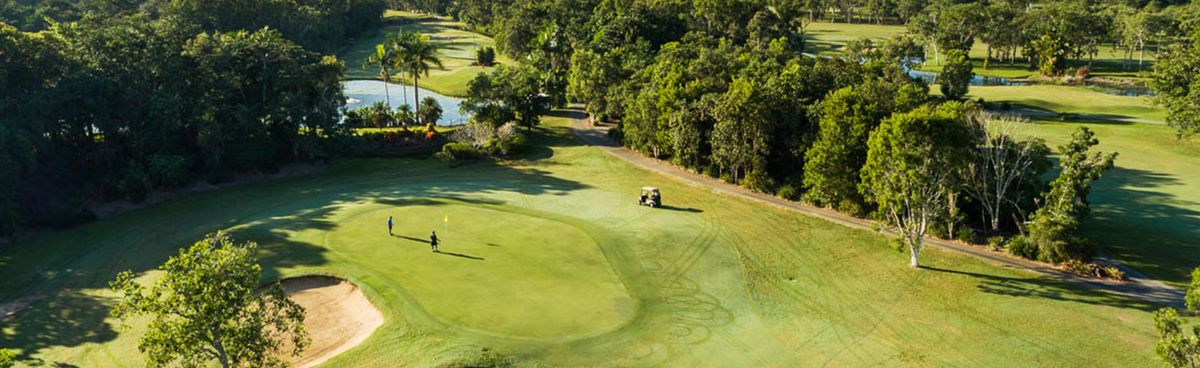 Aerial view of a tropical green at Cairns Golf Club surrounded by lush trees, a lagoon and a golf cart on the path.