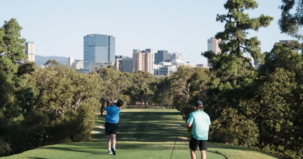 Golfers teeing off at North Adelaide Golf Course with the Adelaide city skyline behind