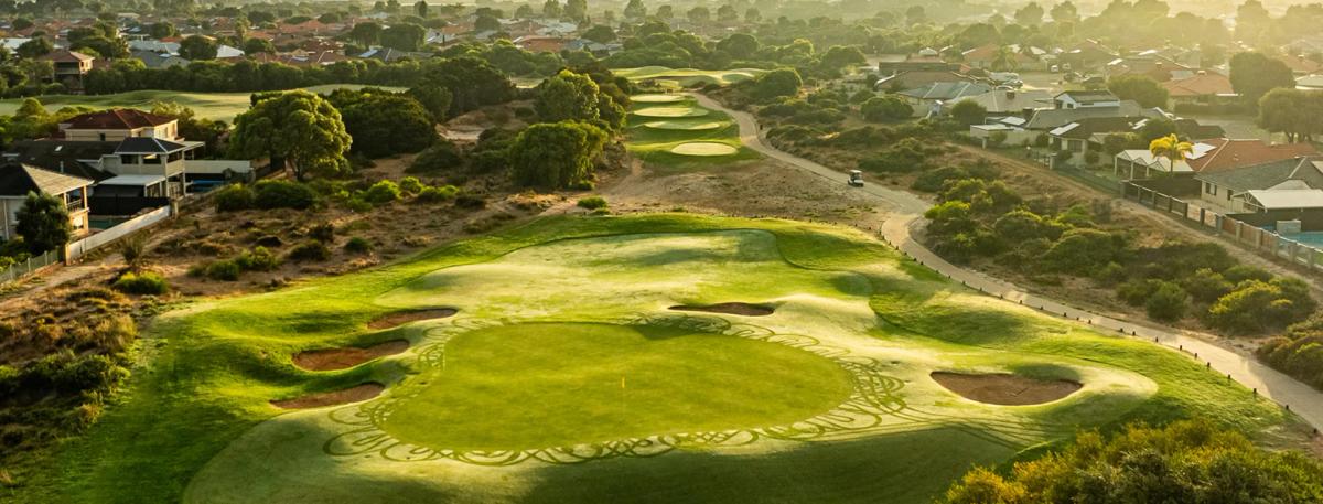 Aerial view of a green surrounded by bunkers at Secret Harbour Golf Links, with the Indian Ocean and coastal suburb in the background.