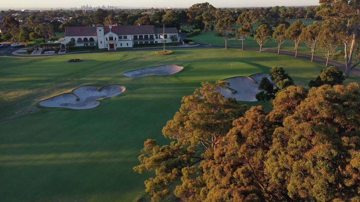 Aerial view of the clubhouse and a bunkered green at Yarra Yarra Golf Club, Melbourne, with the city skyline beyond