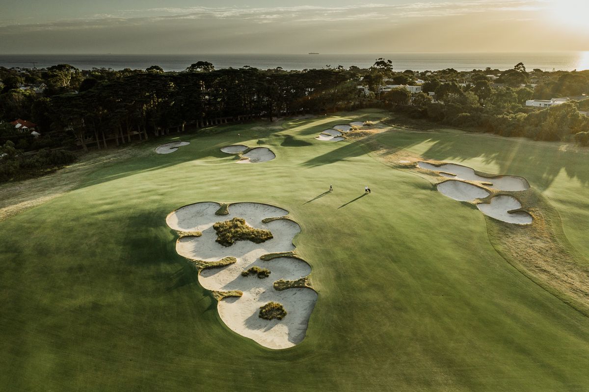The famously sculpted sand-belt bunkers of Royal Melbourne Golf Club at sunset, with Port Phillip Bay in the distance