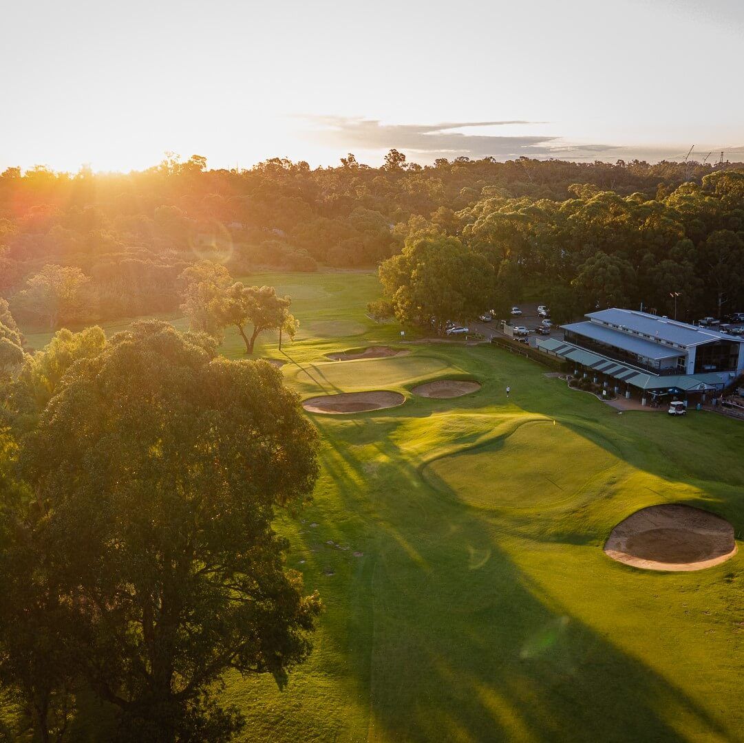 Aerial sunset view of a green with bunkers and the clubhouse at Kwinana Golf Club