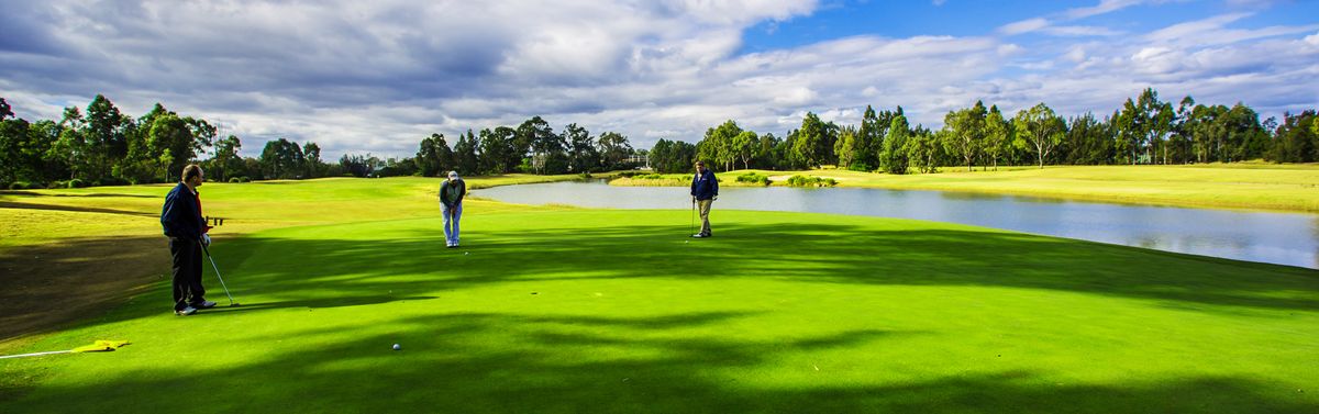 Golfers putting on a green beside a lake at Macquarie Links International Golf Club