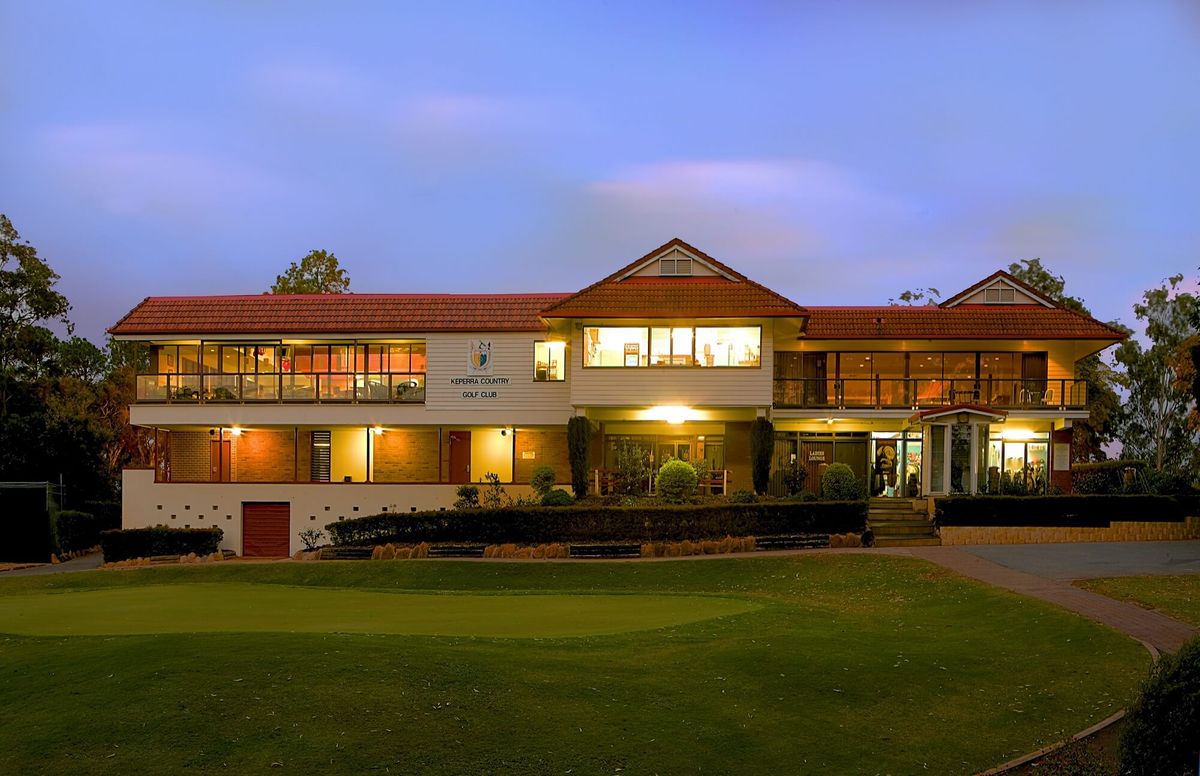 The Keperra Country Golf Club clubhouse lit up at dusk, viewed from the practice green