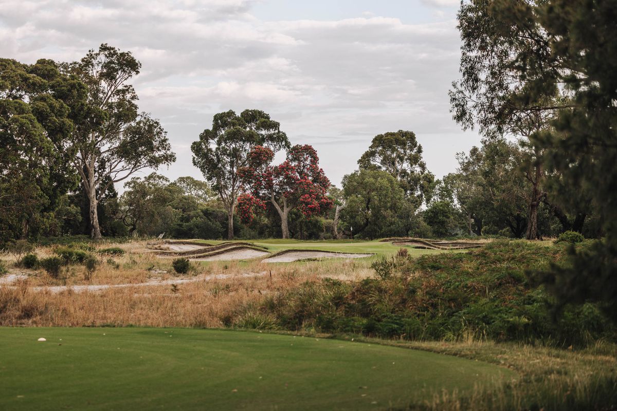 A green guarded by bunkers at Woodlands Golf Club, Melbourne, with flowering gum trees behind