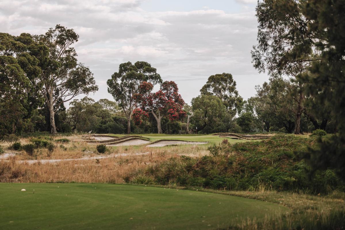 A green guarded by bunkers at Woodlands Golf Club, Melbourne, with flowering gum trees behind