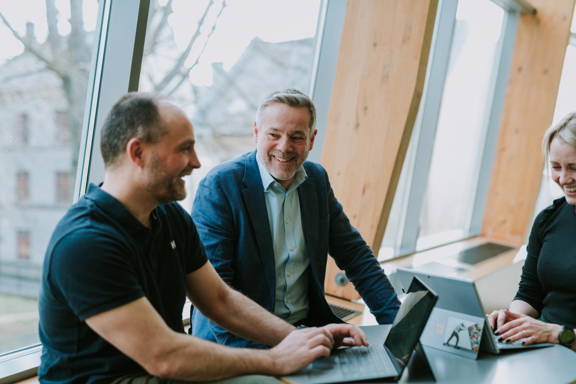 Three Solwr employees smiling and talking while working on their laptops.