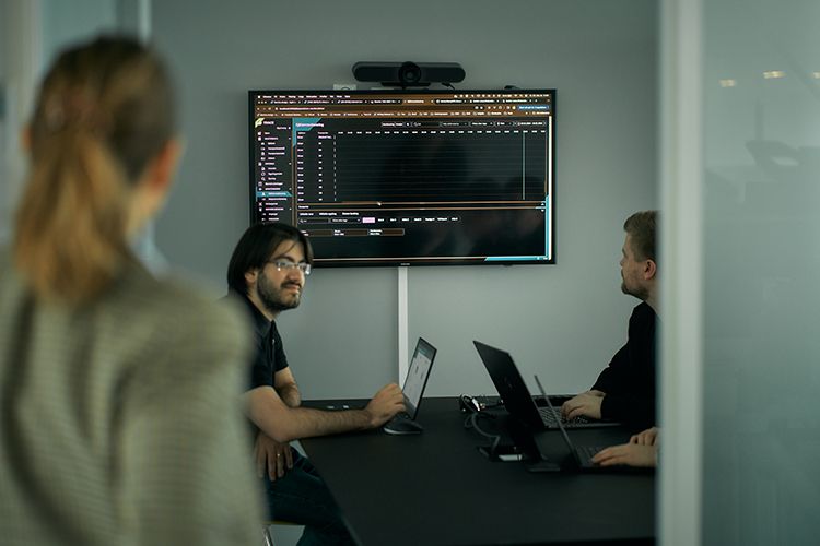 Three Solwr employees, two men working with their PCs and a woman looking at them.