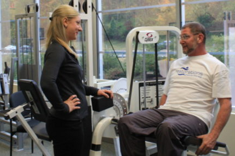 Female physical therapist talking with a male patient on gym equipment