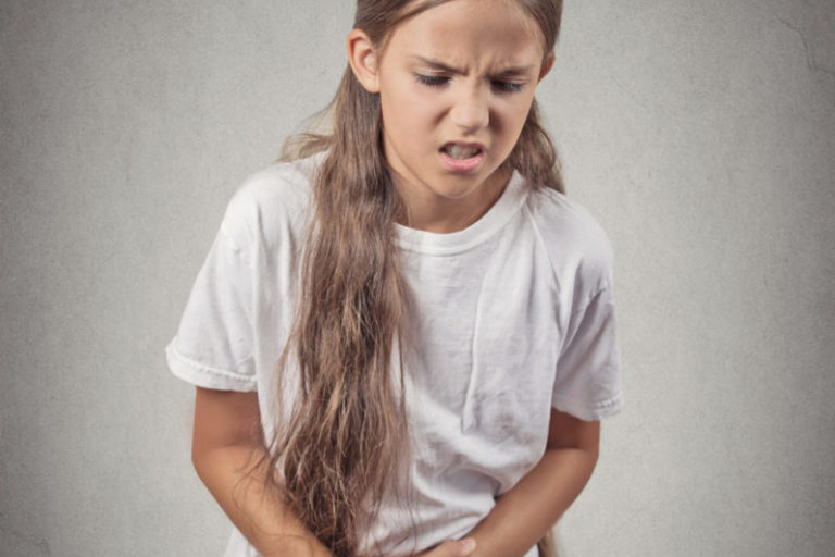 Young girl in agonizing pain with arms crossed over stomach