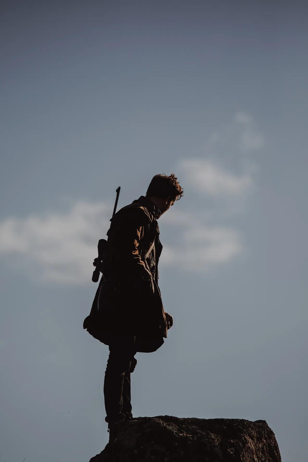 A man atop a hill with hunting gear and a hunting rifle