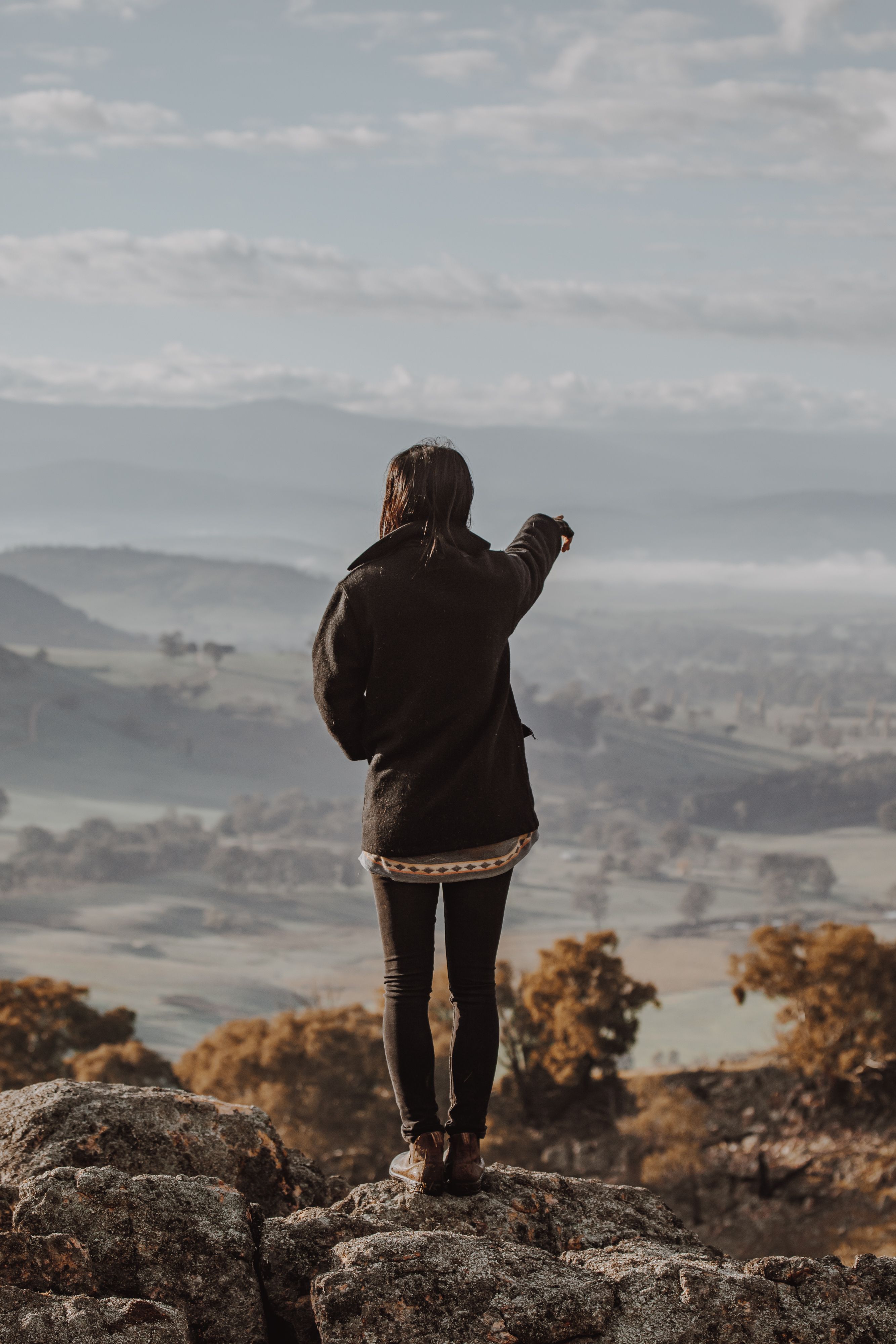 Woman overlooking australian countryside with her back turned, pointing into the distance