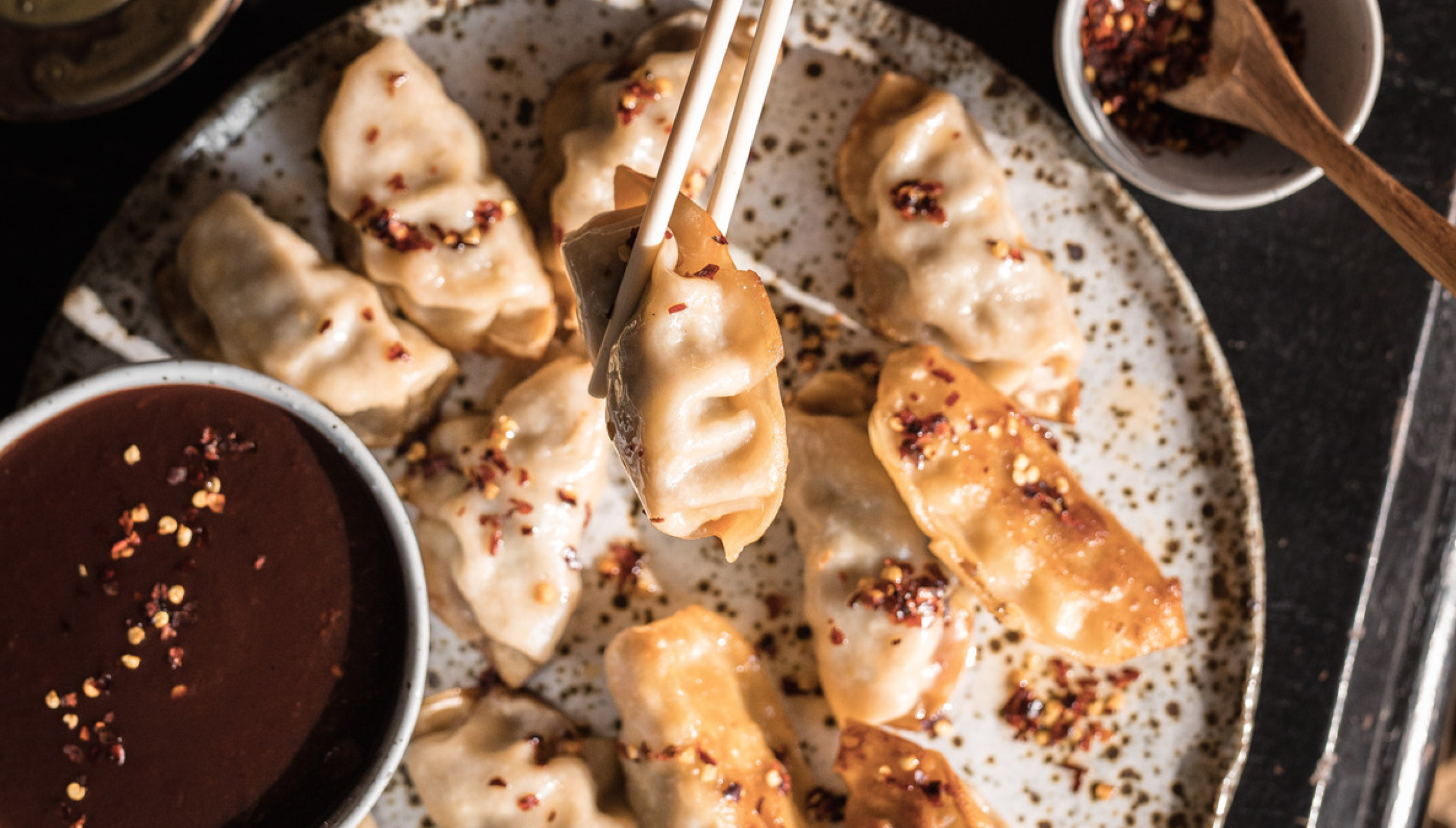 Dumplings being held by chopsticks, about to be dipped into plum sauce
