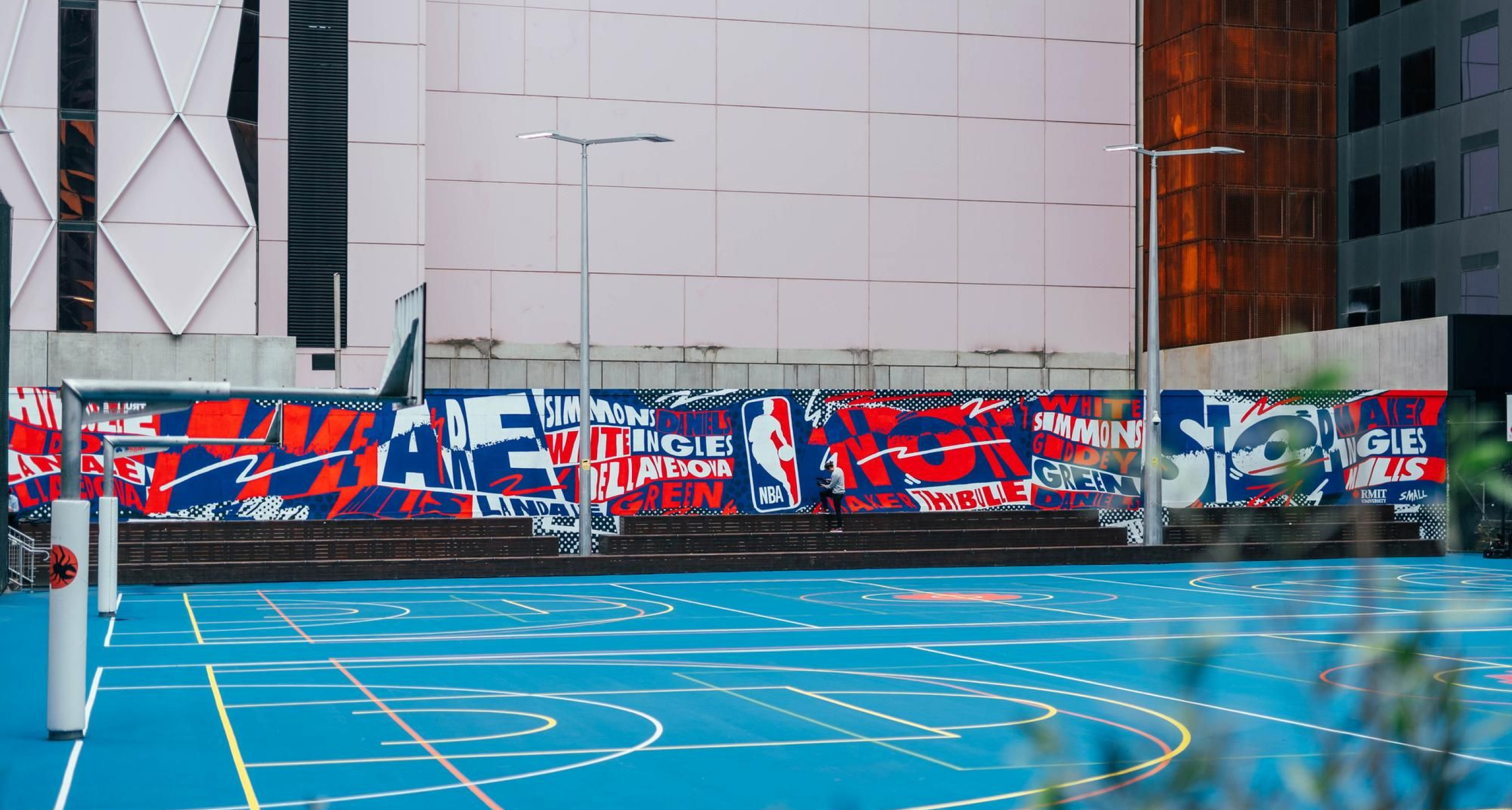 An outdoor basketball court with a painted mural by Kris Andrew Small