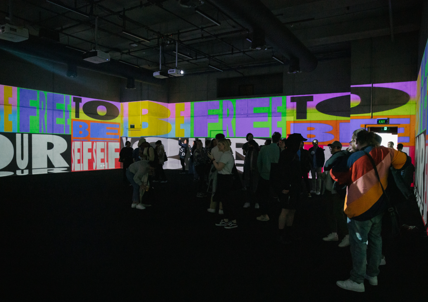 A people filled room entirely covered with brightly coloured artwork projections by Kris Andrew Small