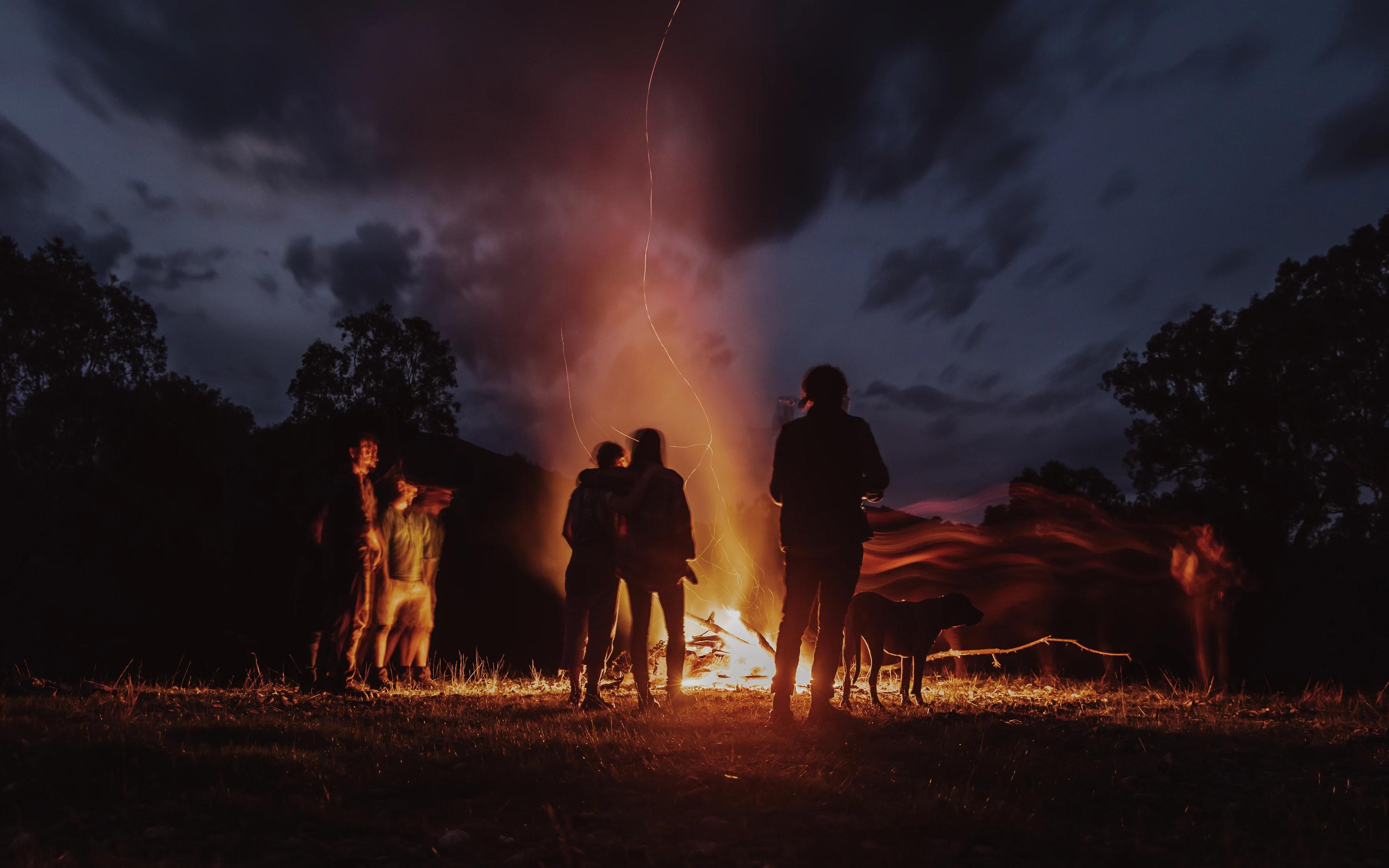 People outside at night smiling around a campfire in the outback