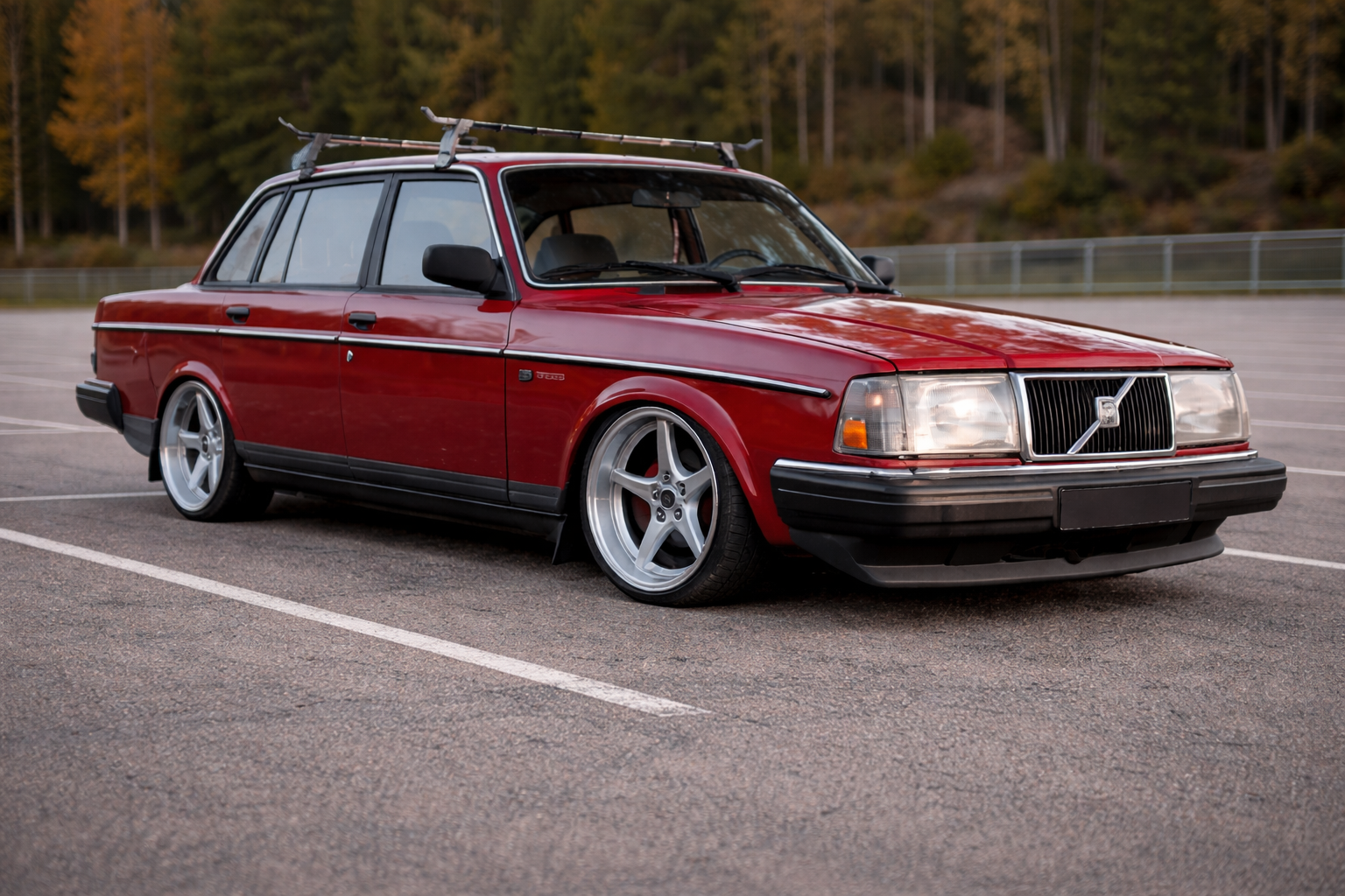 Röd Volvo 240 med silverfärgade MK18 fälgar, fotad snett framifrån på en tom parkering