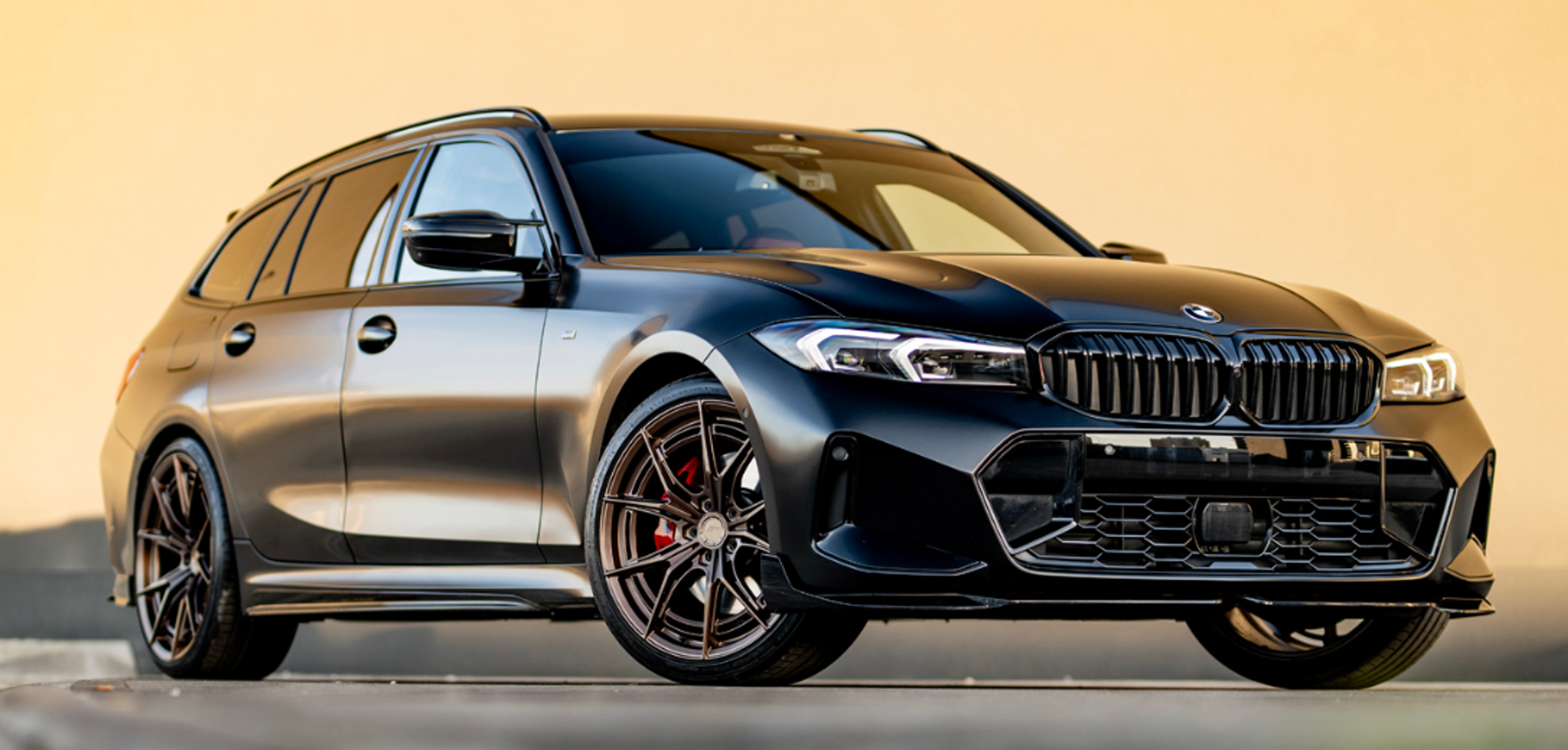 Svart BMW Touring med mörka JR50 fälgar och rött bromsok mot kvällshimmel