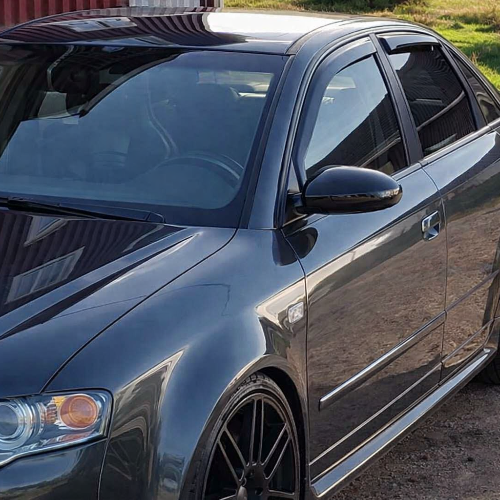Audi A4 snett framifrån på förarsidan i dagsljus, med tonade rutor, svarta fälgar och tydliga vindavvisare ovanför sidorutorna.