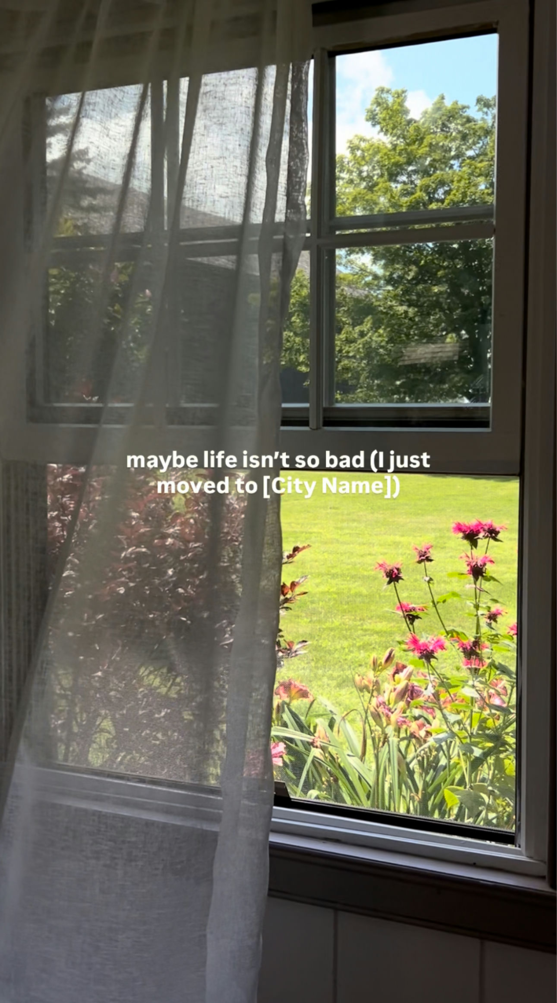 View through a window showing green lawn and flowers outside with overlay text reading, “maybe life isn’t so bad (just moved to [City Name]).”