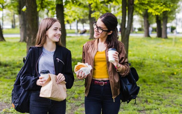 Twee collega's wandelen en praten in het park met koffie en een broodje