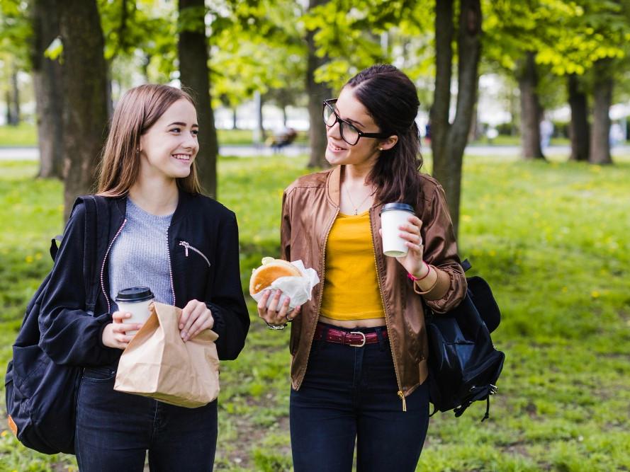 Twee collega's wandelen en praten in het park met koffie en een broodje