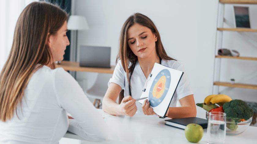Twee vrouwen bespreken een voedingsschema aan een tafel vol groente en fruit