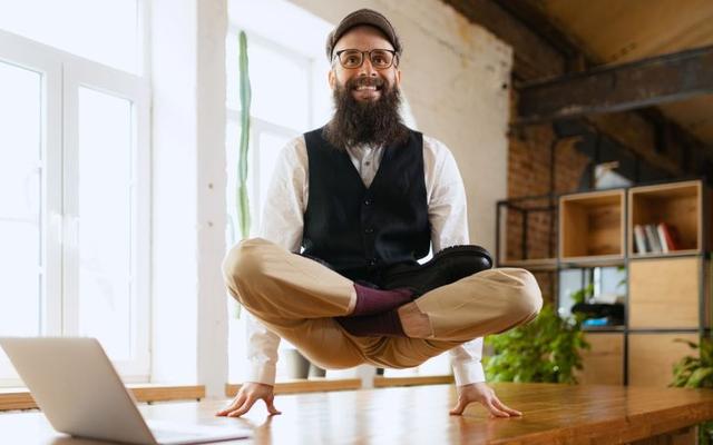 A person is meditating in a seated position, levitating above a table in a bright, modern room.