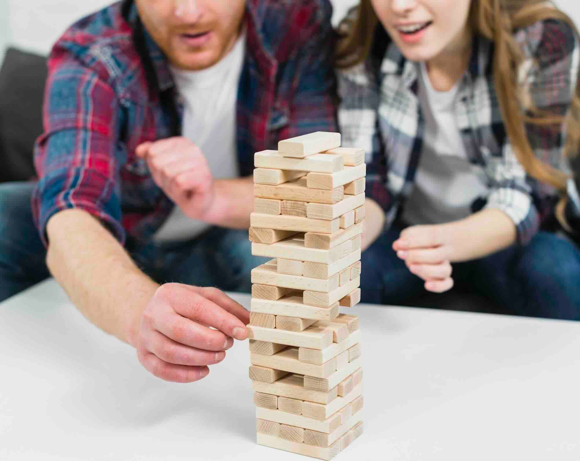 A man and a woman playing Jenga, carefully pulling out a block from a tall stack.