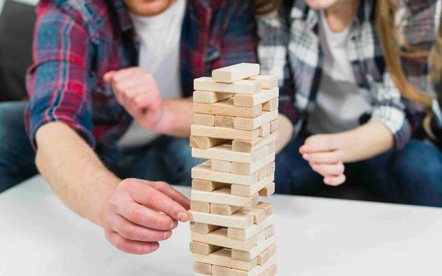 A man and a woman playing Jenga, carefully pulling out a block from a tall stack.