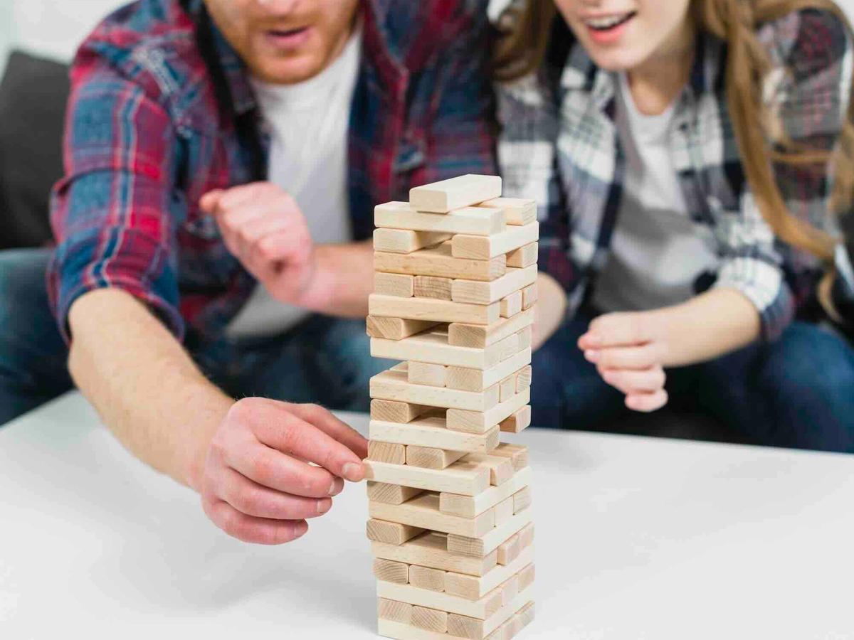 Een man en een vrouw spelen Jenga en trekken voorzichtig een blok uit de toren