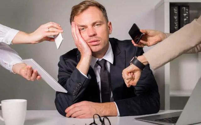 In an office setting, a weary businessman in a suit rests his face on his hand, surrounded by multiple outstretched arms holding a phone, a tablet, a document, and a watch, symbolizing overwhelming demands and stress.