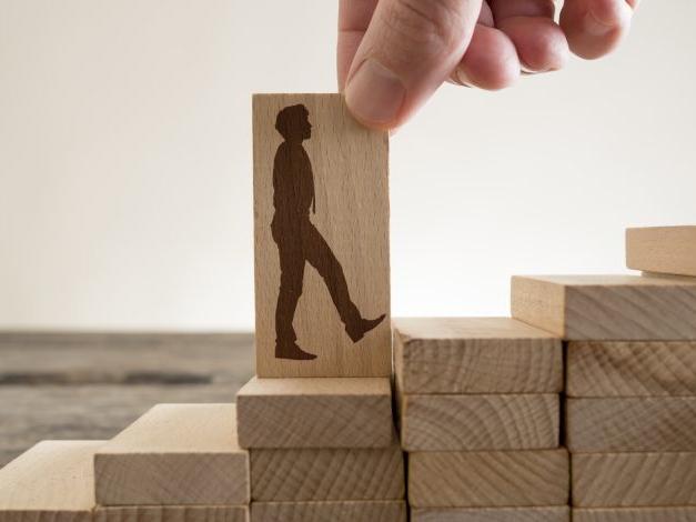 Man holding with his fingers wooden domino with shape of business man walking up
