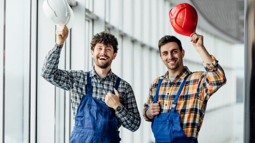 Good looking construction workers sharing experience and they are holding their helmets up. They are looking happy