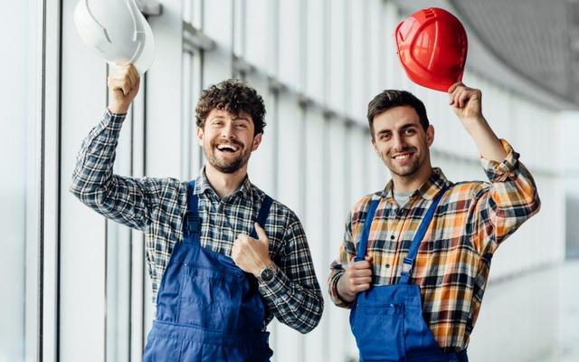 Good looking construction workers sharing experience and they are holding their helmets up. They are looking happy