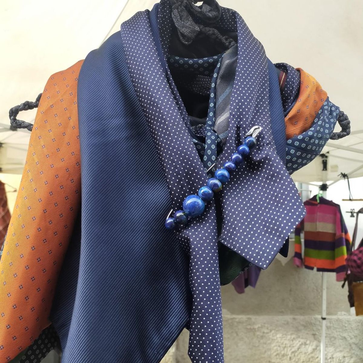 Stola di cravatte blu a pois e arancio, chiusa con una spilla di perle blu, appesa a un appendiabiti