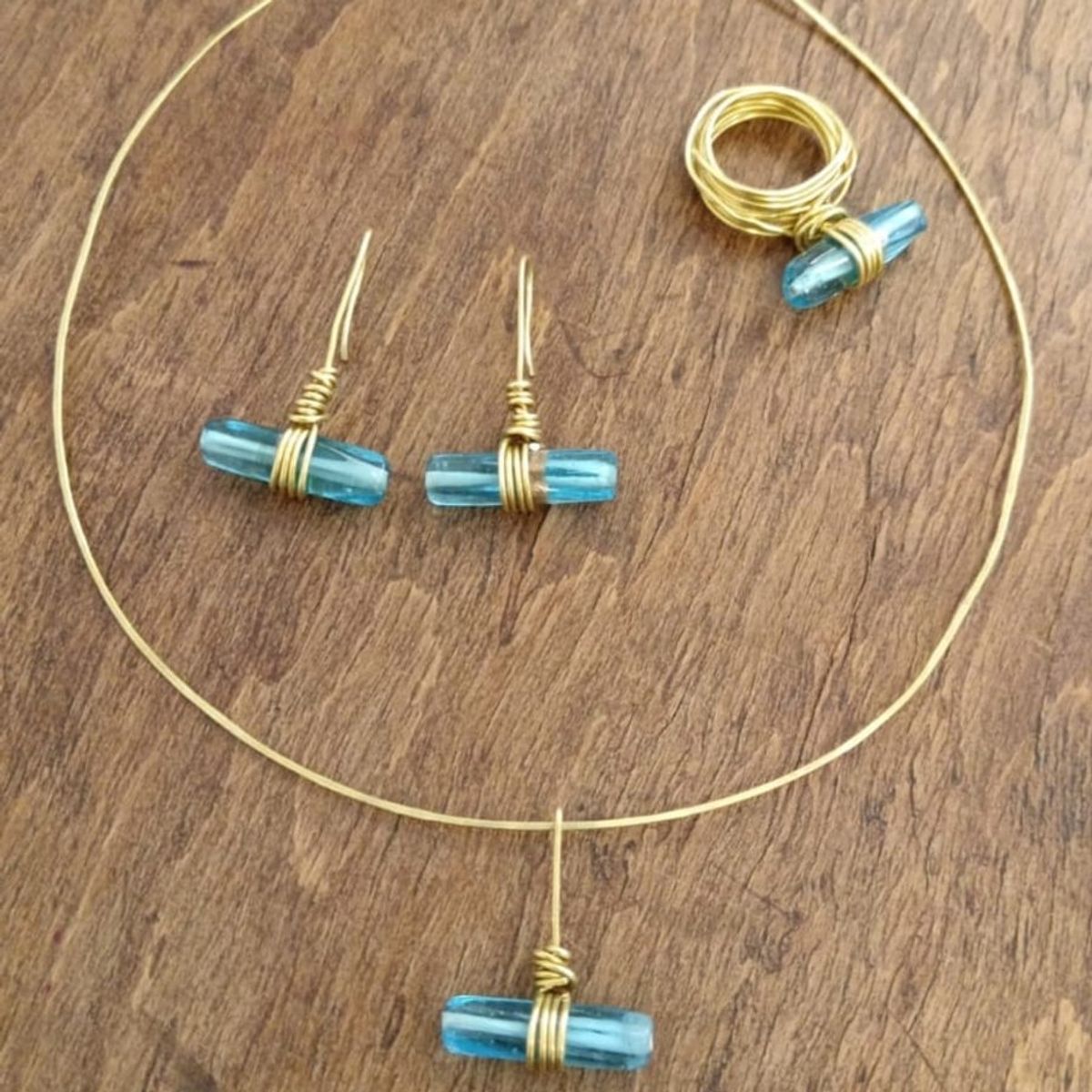 Parure in ottone con cristalli di vetro azzurri: collier con ciondolo, orecchini e anello su un tavolo di legno