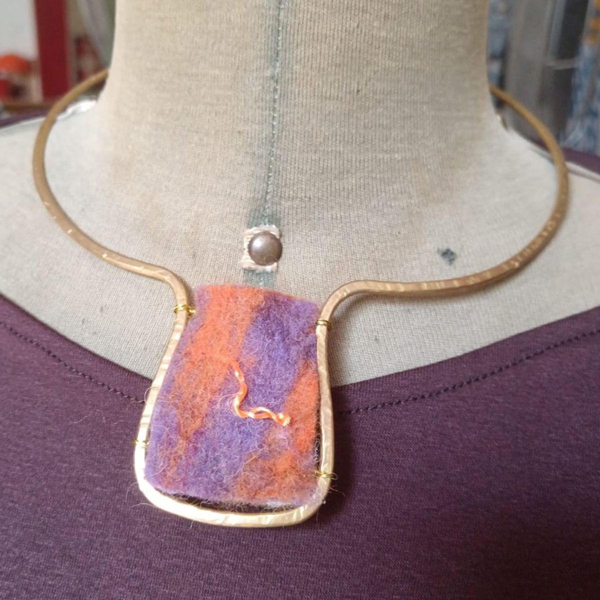Collier in ottone con un pannello di feltro viola e arancio, indossato su un manichino