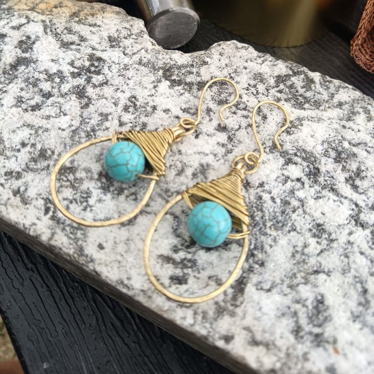 Coppia di orecchini a goccia in ottone con una pietra howlite turchese, appoggiati su una pietra grigia