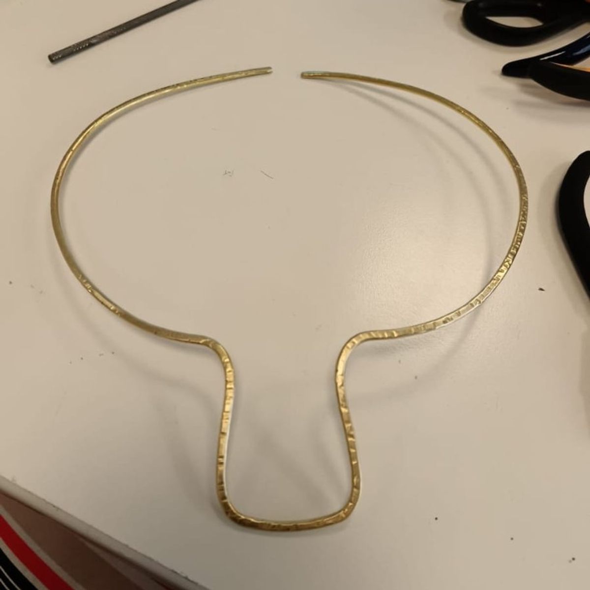 Collier rigido in filo di ottone martellato, appoggiato su un tavolo bianco