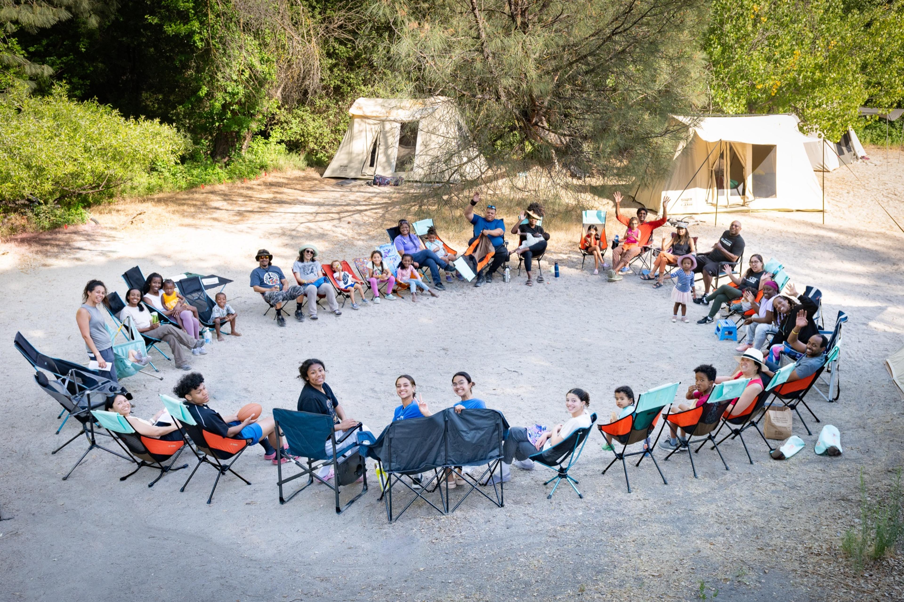 About forty people gathered in a circle of camp chairs on sand with canvas tents behind them at Pinnacles National Park