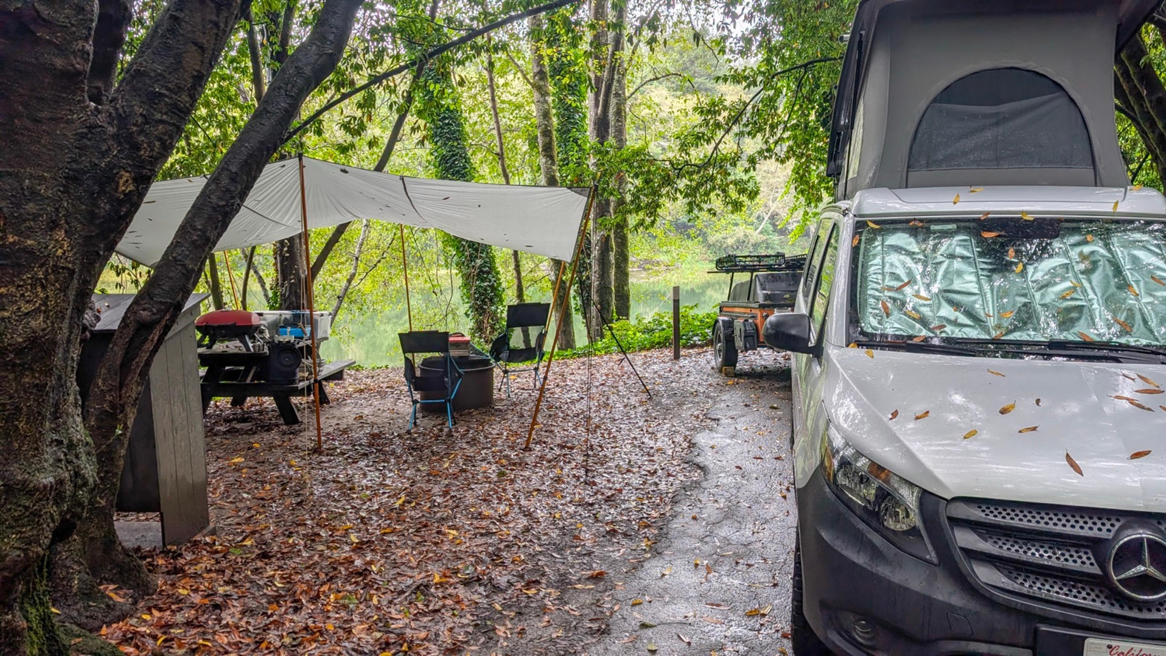 Tarp strung over a picnic table beside a camper van at Gualala Point Regional Park, wet leaves on the ground and the Gualala River behind Tarp strung over a picnic table beside a camper van at Gualala Point Regional Park, wet leaves on the ground and the Gualala River behind