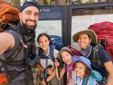 The Steele family wearing backpacking packs and smiling at the Kings Creek trailhead sign in Lassen Volcanic National Park