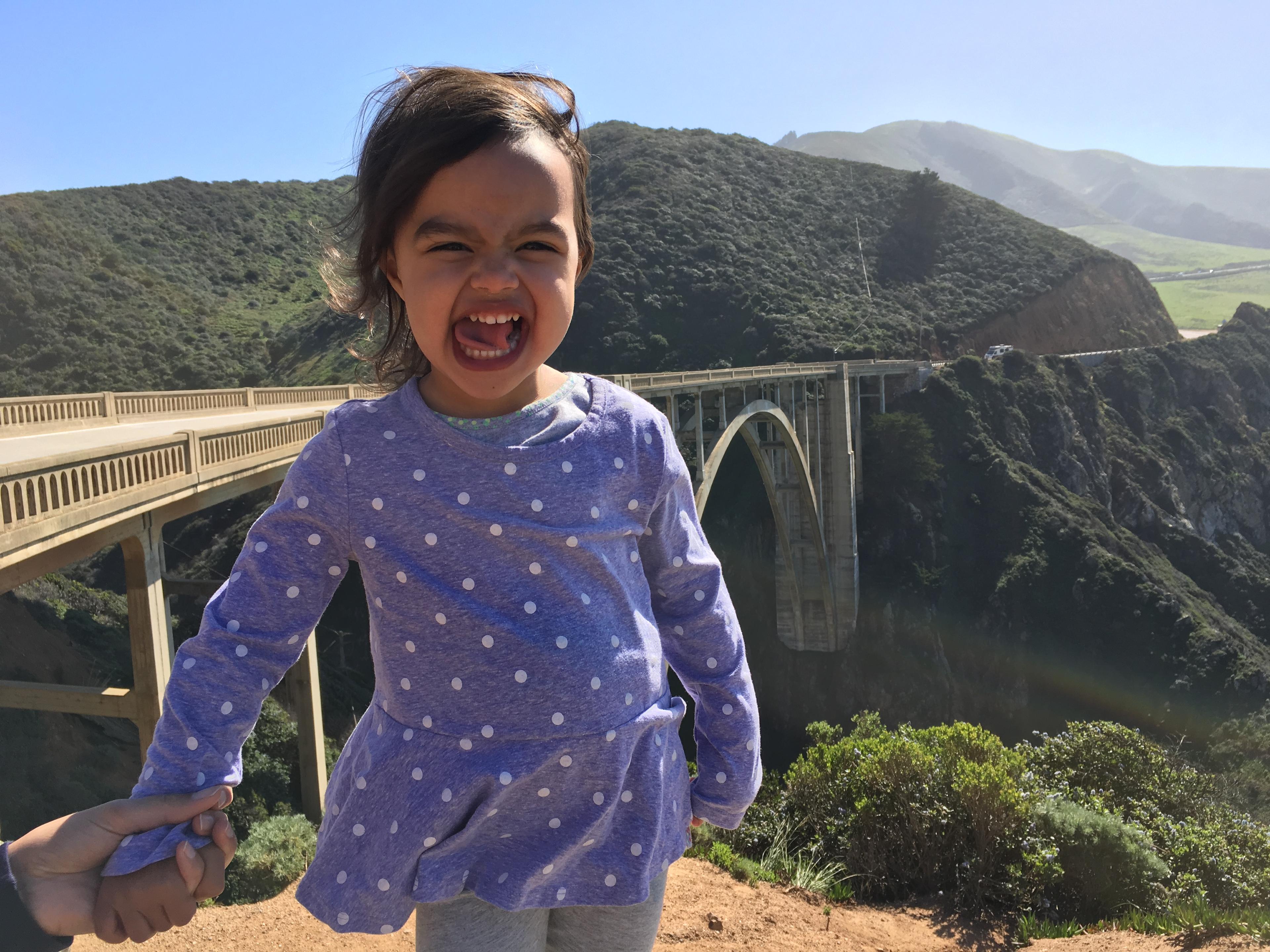 Zadie laughing in front of Bixby Bridge on Highway 1 with green hills behind her Zadie laughing in front of Bixby Bridge on Highway 1 with green hills behind her