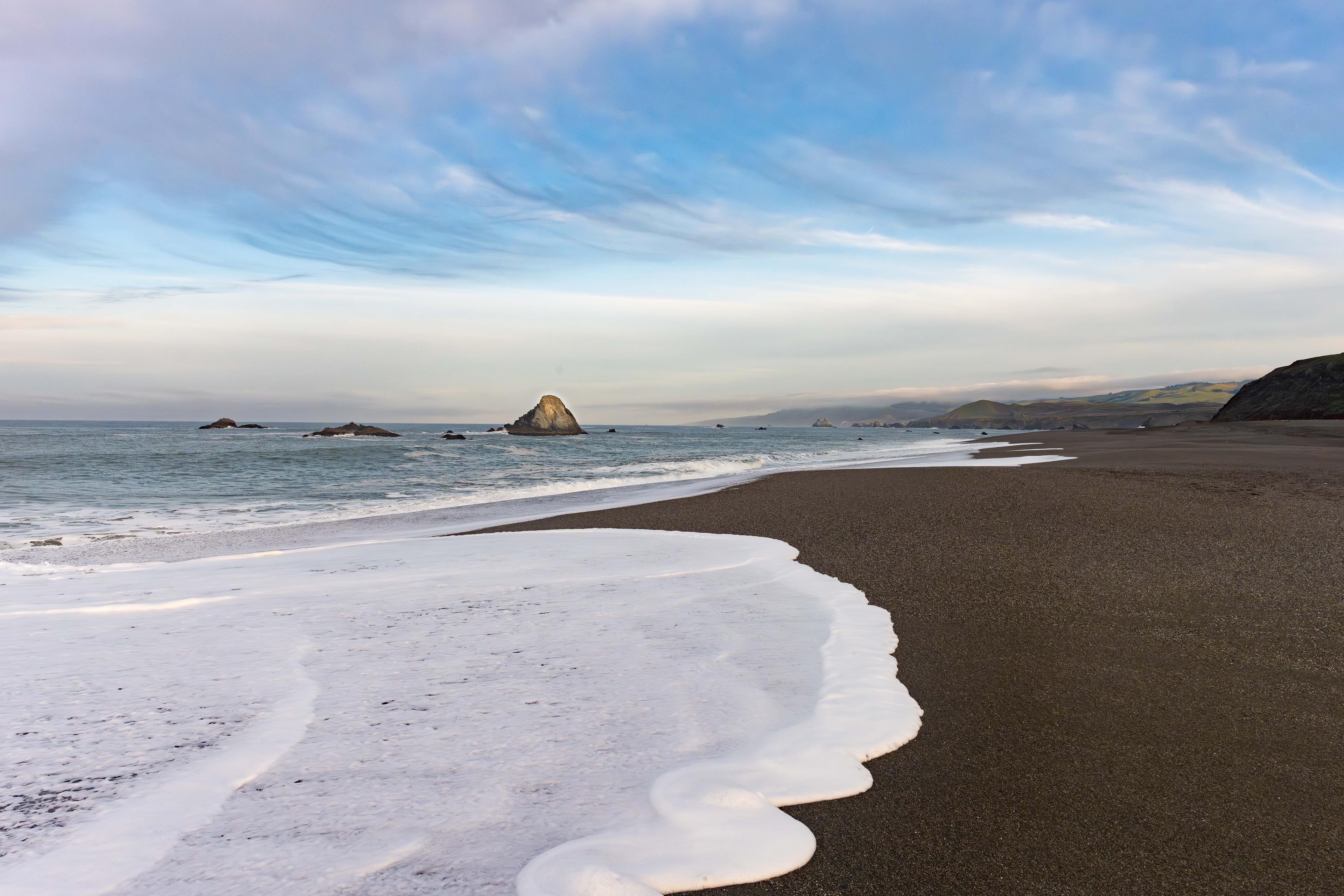Dark sand beach at Wright's Beach on the Sonoma Coast with sea stack and white foam from waves Dark sand beach at Wright's Beach on the Sonoma Coast with sea stack and white foam from waves